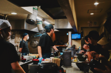 Chefs preparing Japanese dishes in a busy open restaurant kitchen.