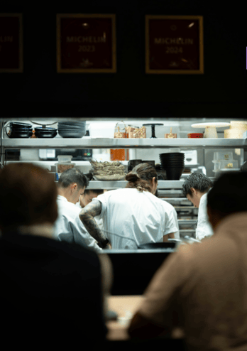Restaurant chefs working beneath Michelin Guide award plaques in an open kitchen.