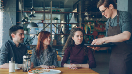 Server presenting a meal to guests at a casual restaurant table.