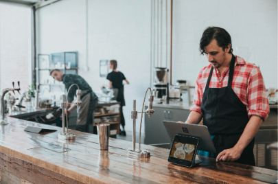 Barista using a POS tablet behind the ordering counter in a bright specialty coffee shop.